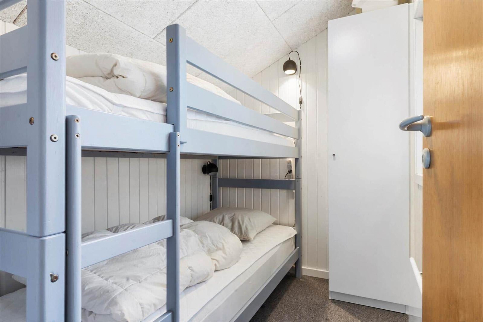 Zimmer mit Doppelstockbett, weißer Schrank und Wandlampe.