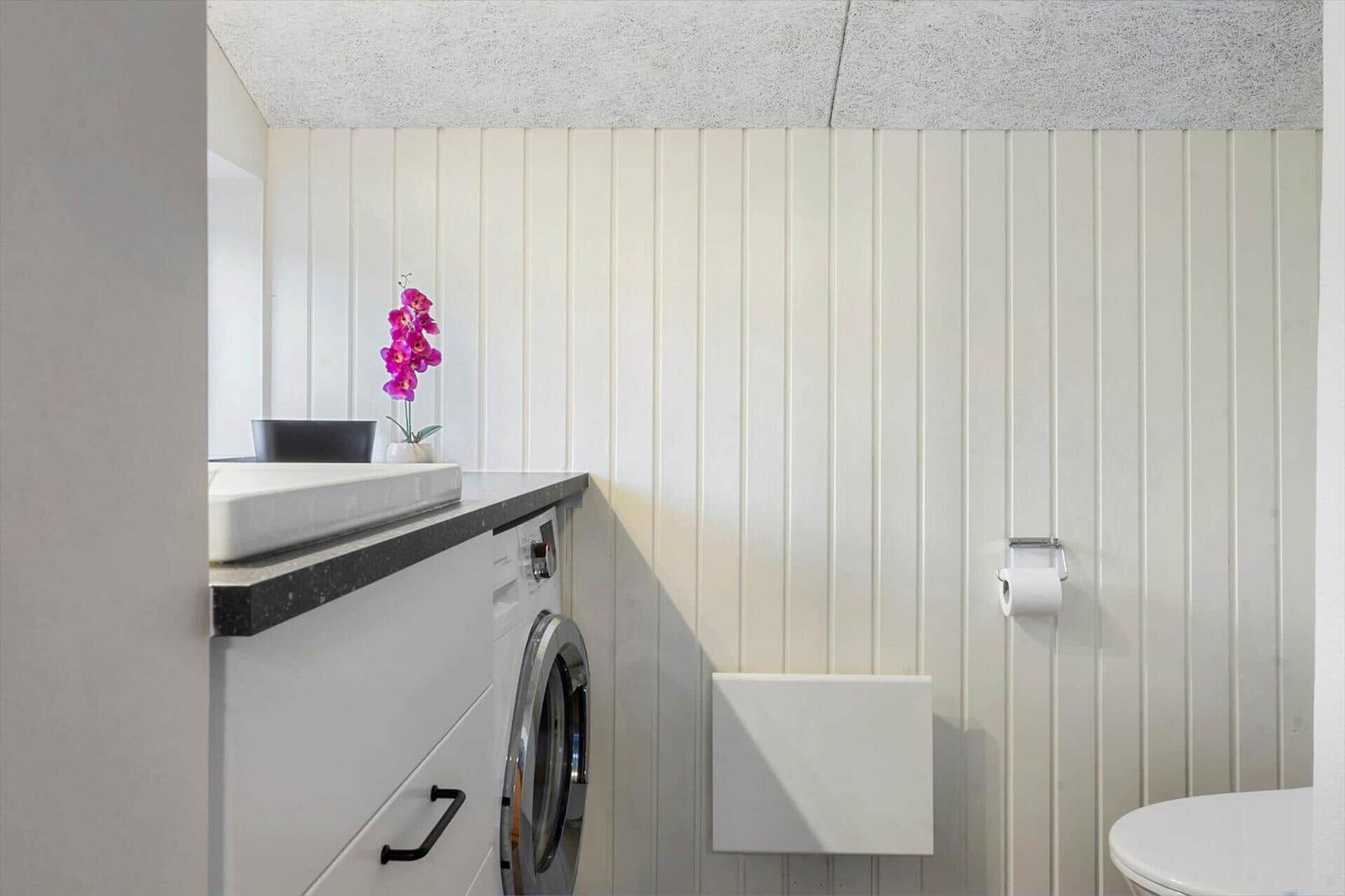 Badezimmer mit Waschmaschine, Spülbecken und Toilette. Wandverkleidung und Decke sichtbar.