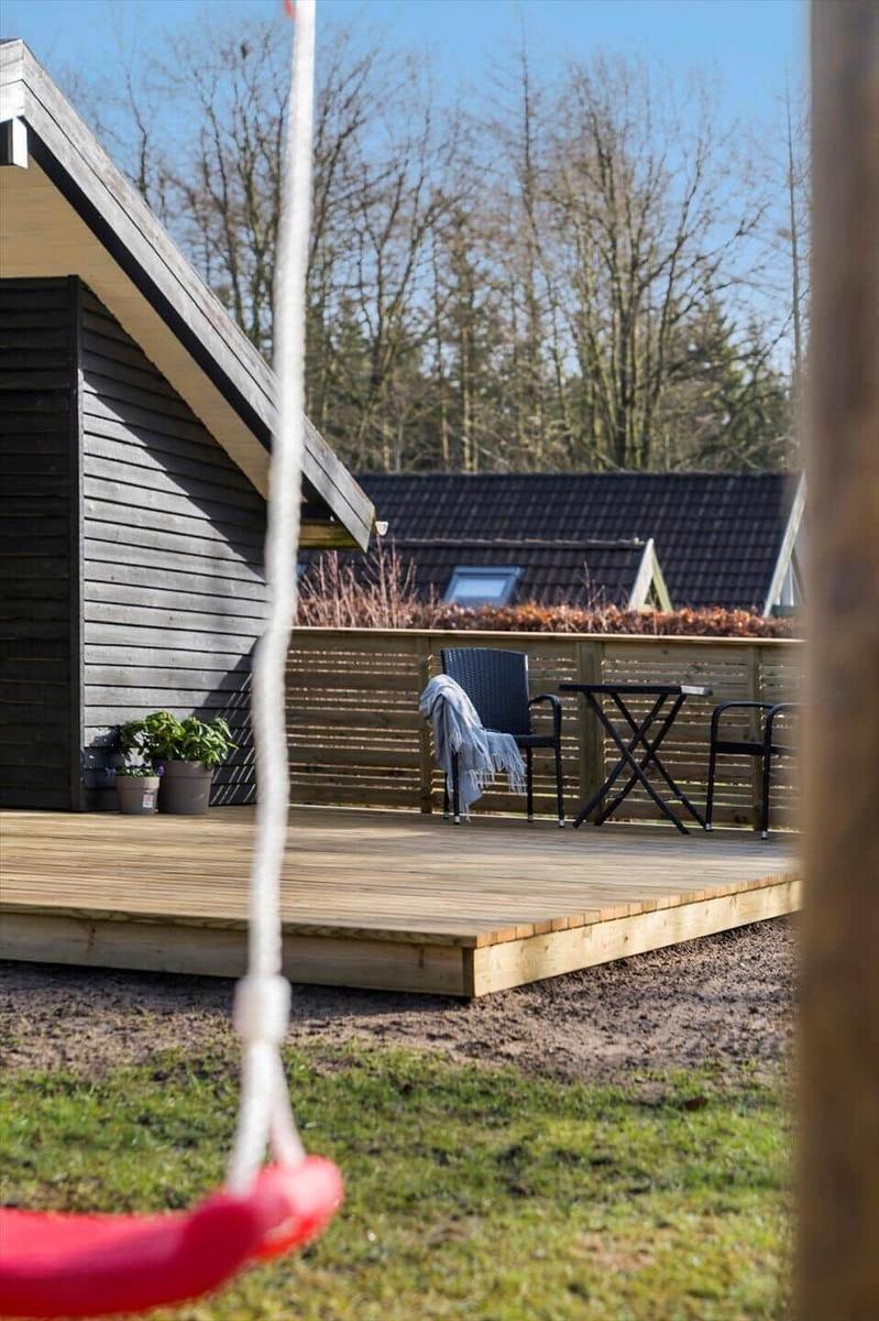 Hinter einem roten Schaukelhängematt steht eine Terrasse mit Tisch und Stühlen.