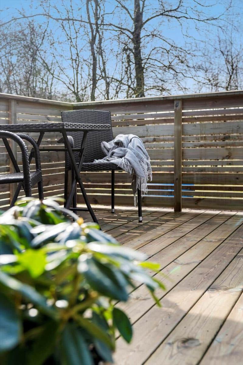Terrasse mit Tisch, Stühlen und Decken. Holzgeländer und Bäume im Hintergrund.