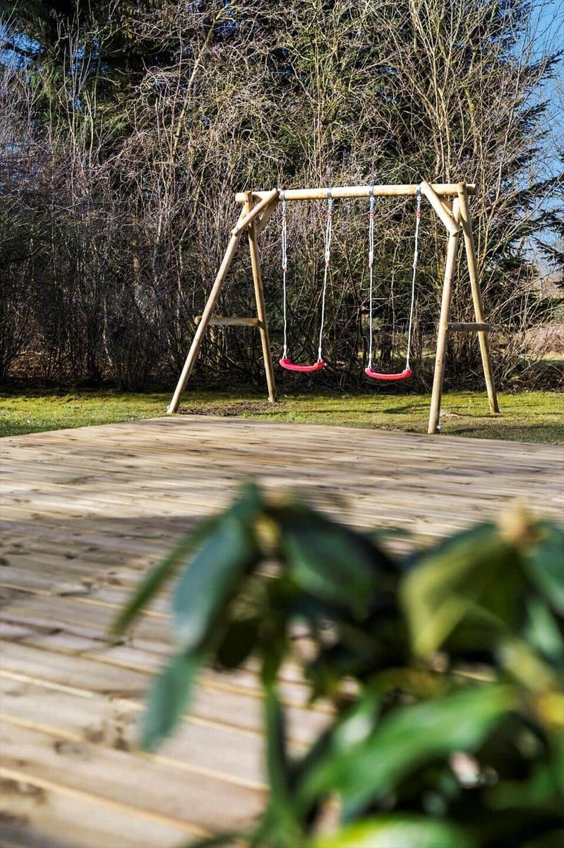 Holzschaukel mit zwei Sitzplätzen auf einer Terrasse im Garten.
