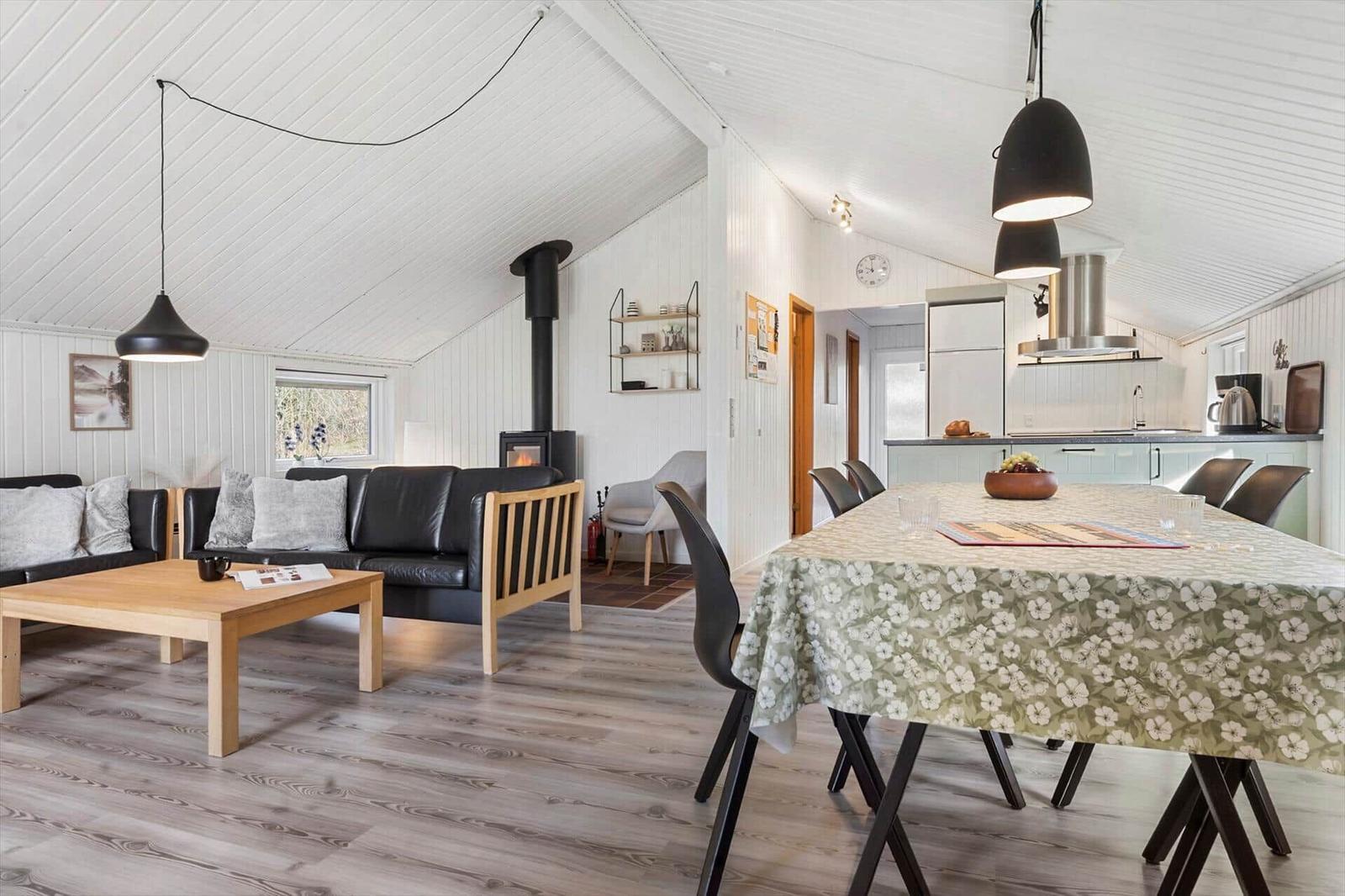 Wohn- und Essbereich mit Holzboden, schwarzer Couch und Esstisch mit Tischdecke.