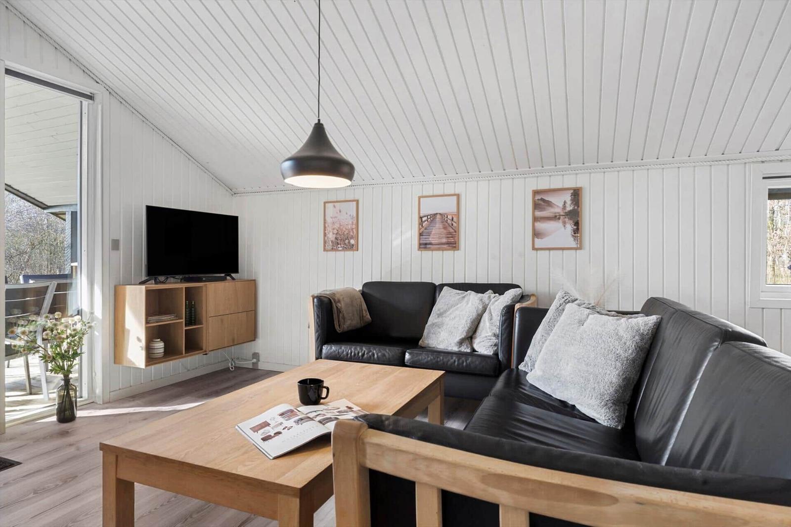 Wohnzimmer mit schwarzer Couch, Holztisch und TV an der Wand.