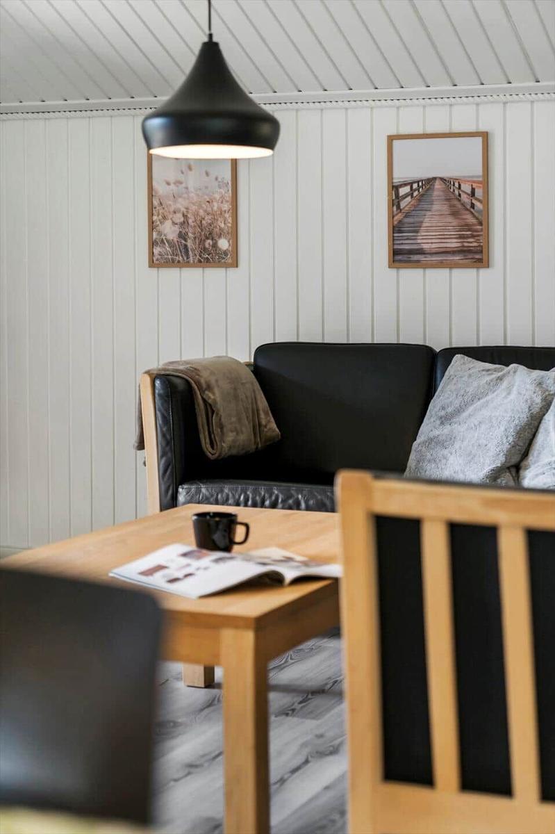 Ein Wohnzimmer mit schwarzer Ledercouch, Holztisch und Wandbildern.