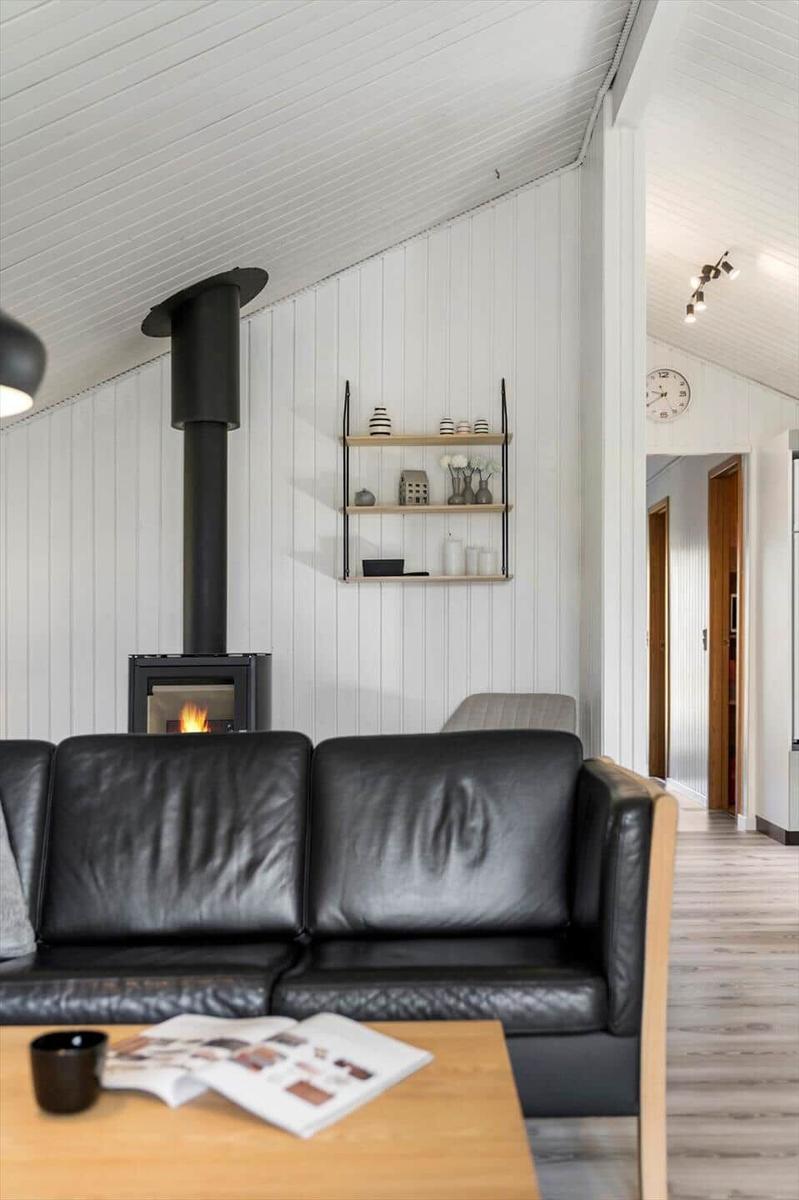 Schwarzes Ledersofa vor Kamin mit Holzregal und weißen Wänden.