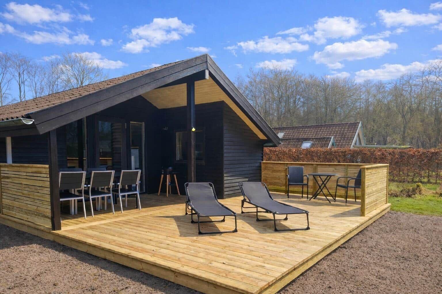 Holzterrasse mit Liegen, Tischen und Stühlen vor einem modernen Holzhaus.