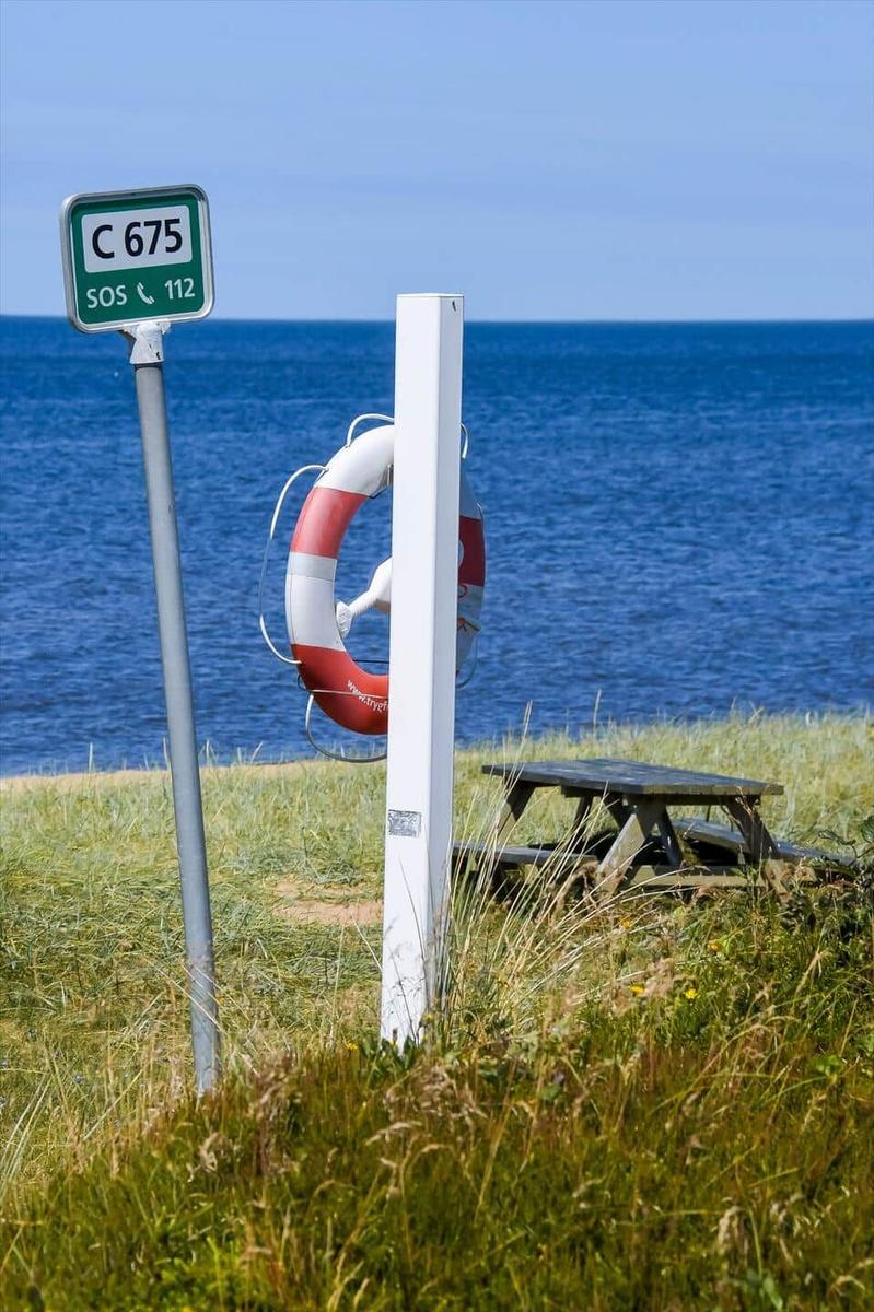 Schild mit C 675 und Rettungsring an Strand. Picknicktisch im Hintergrund.