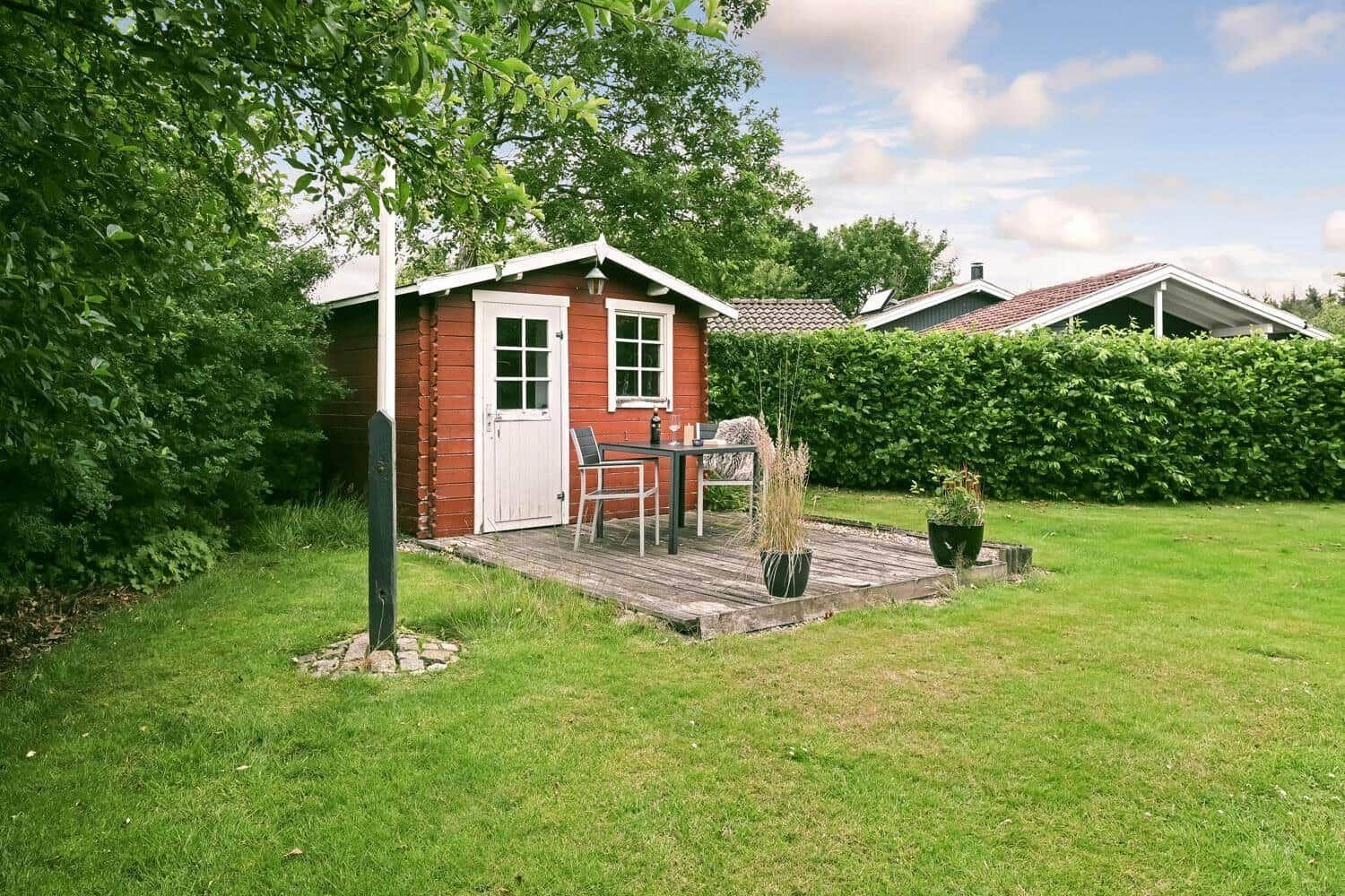 Rotes Holzhaus mit Terrasse, Tisch, Stühlen und Pflanzen im Garten.