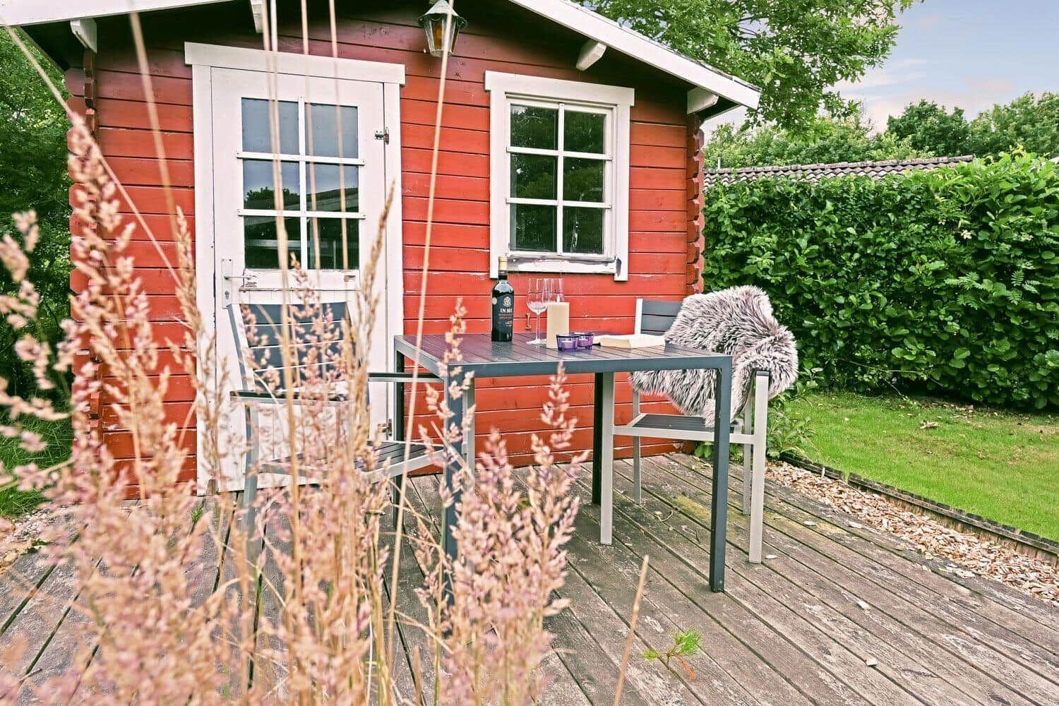Roter Holzschuppen mit Terrasse, Tisch und Stühlen im Garten.