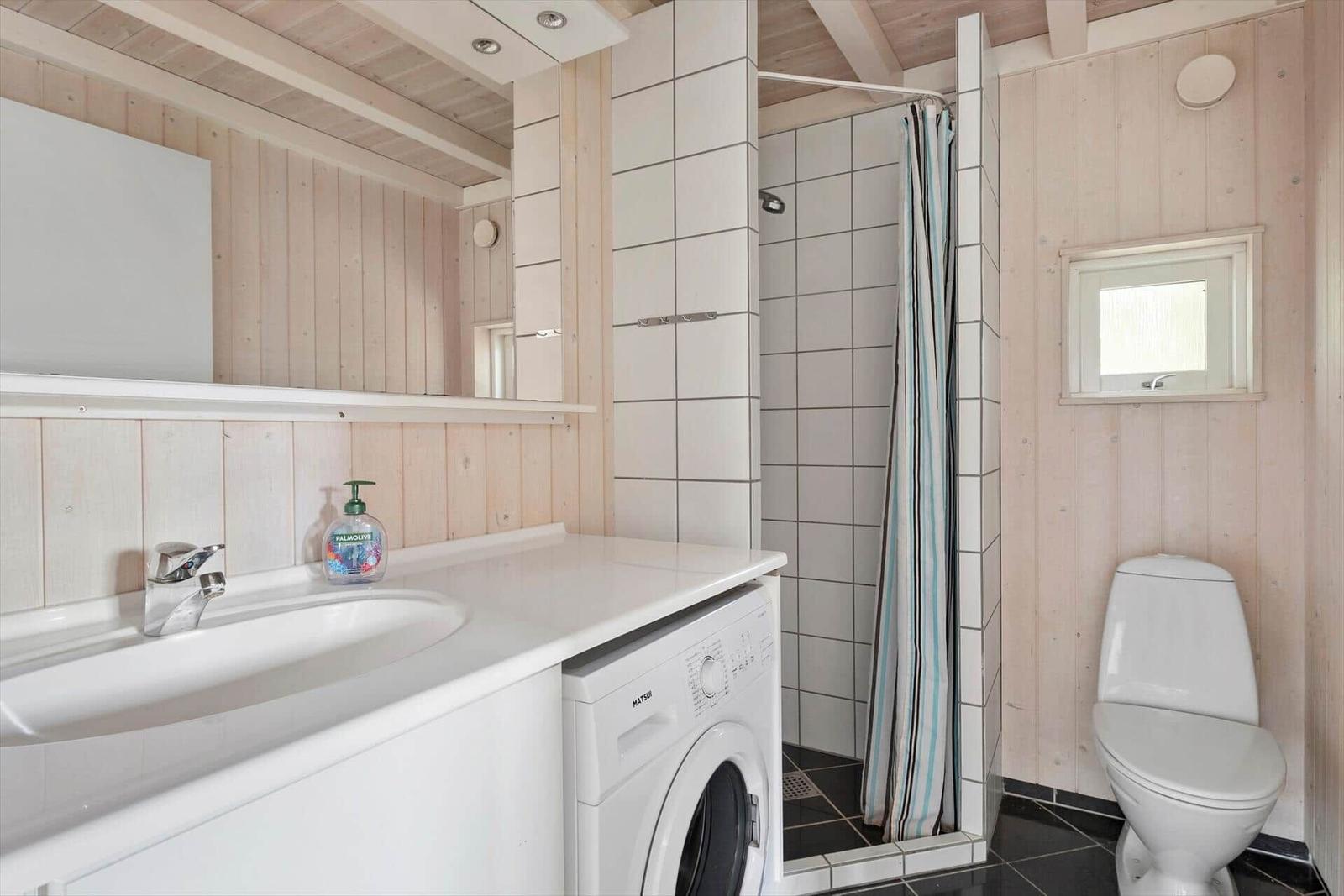 Badezimmer mit Dusche, Waschmaschine und Toilette.