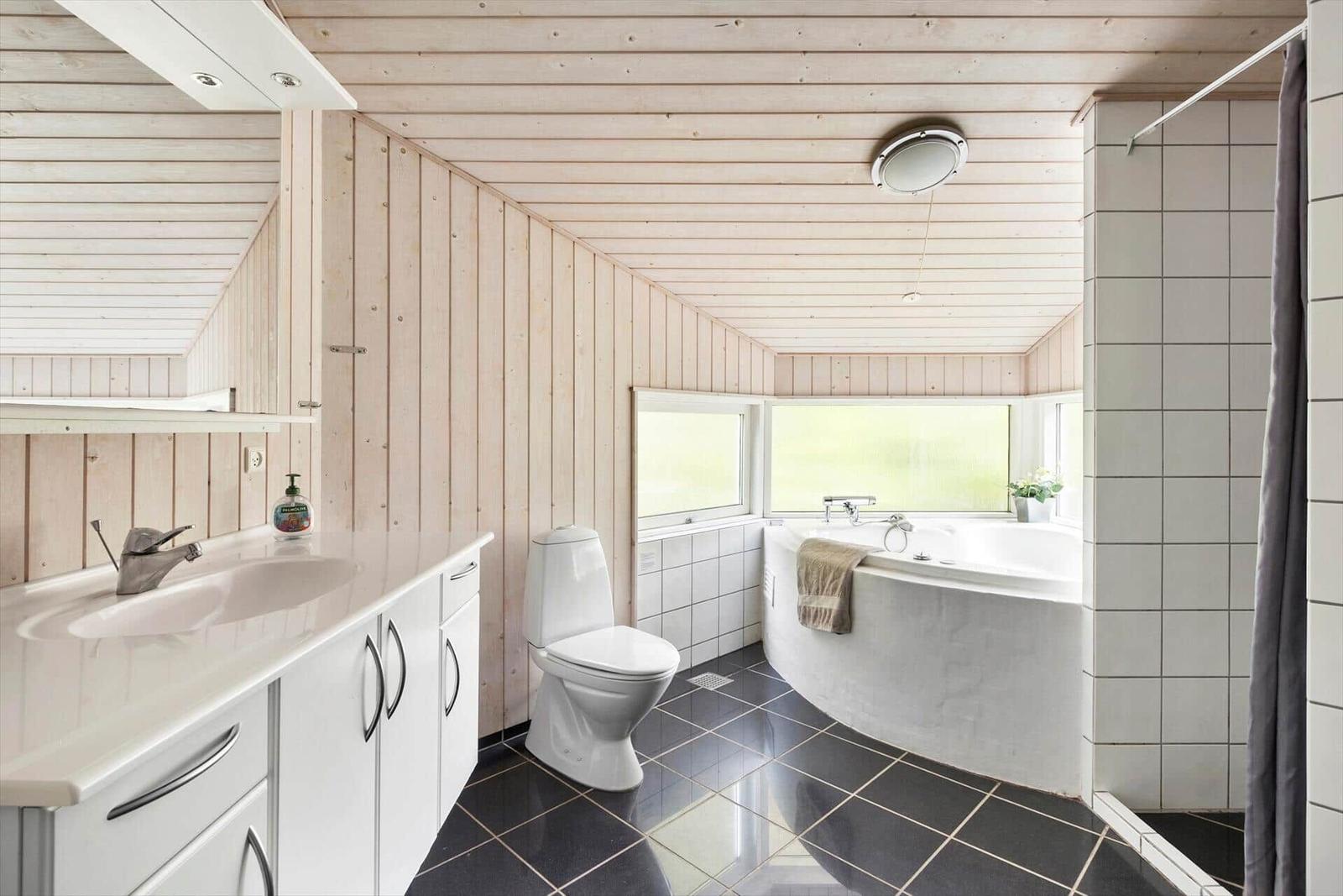 Badezimmer mit Dusche, Badewanne und Toilette. Holzwände und Fliesenboden.