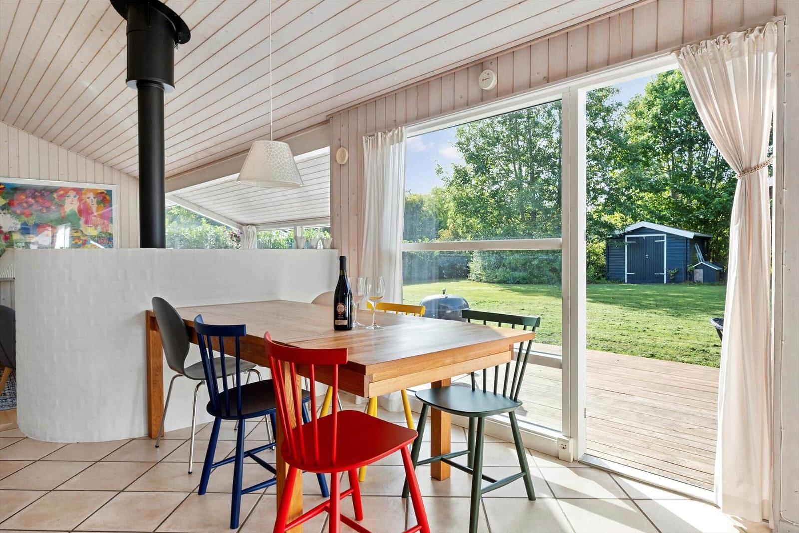 Essbereich mit Tisch, bunten Stühlen und Blick auf Garten.