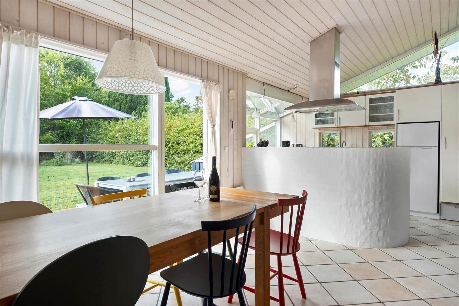 Essbereich mit Holztisch und Stühlen, Küche mit Kücheninsel und Blick auf Garten.