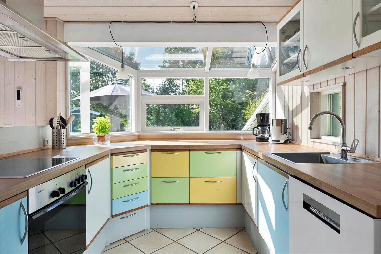 Küche mit farbigen Schubladen, Holzoberflächen und großem Fenster zur Außensicht.