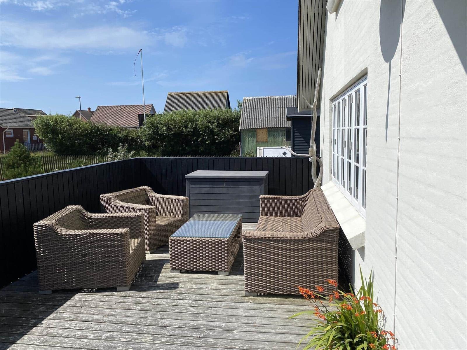 Terrasse mit Sitzgruppe, Tisch und Holzdecke. Hintergrund: Wohnhäuser und Hecke.