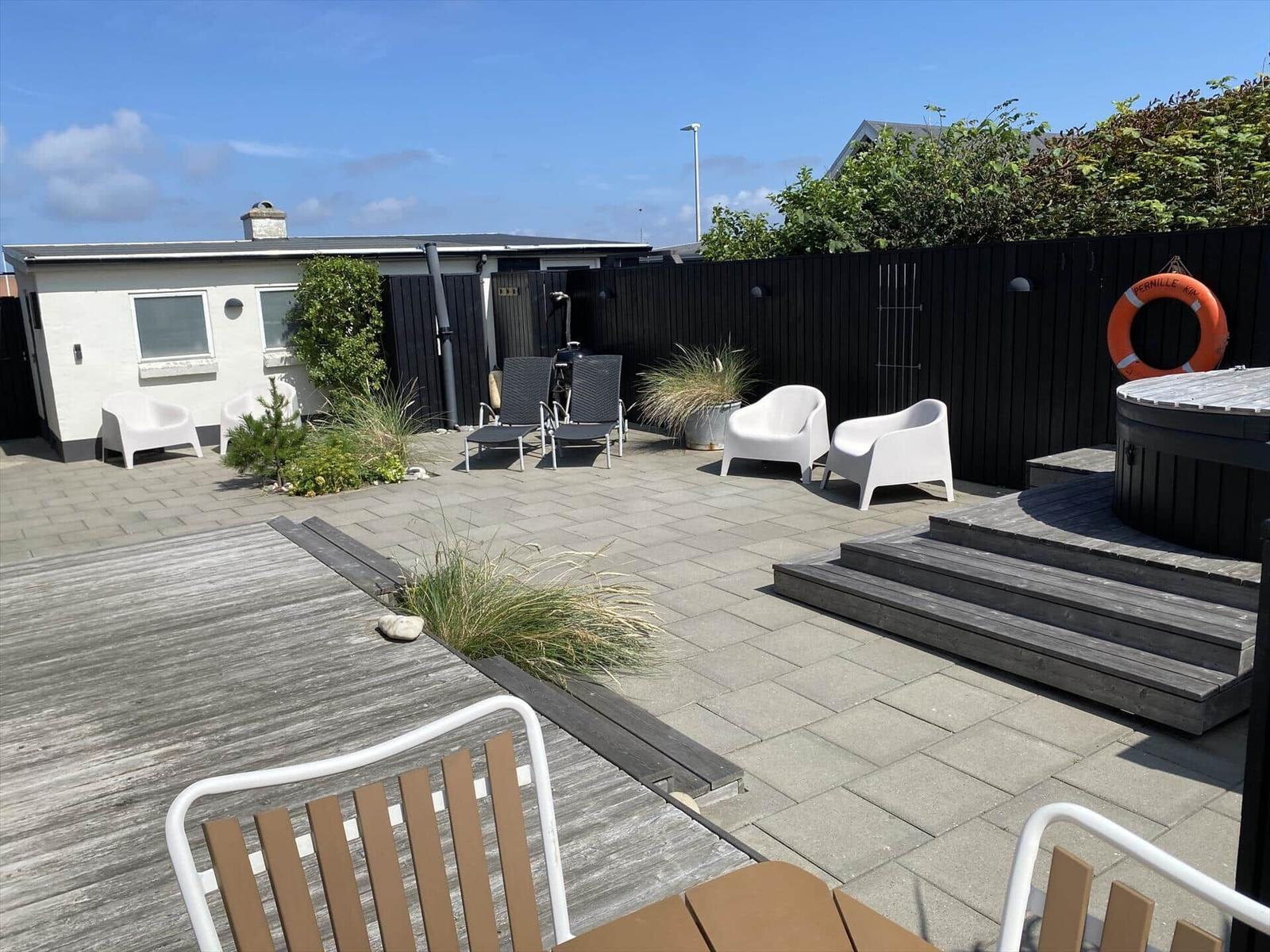 Terrasse mit Sitzgelegenheiten, Whirlpool und Pflanzen. Hinterhof mit Holzzaun und Garten.