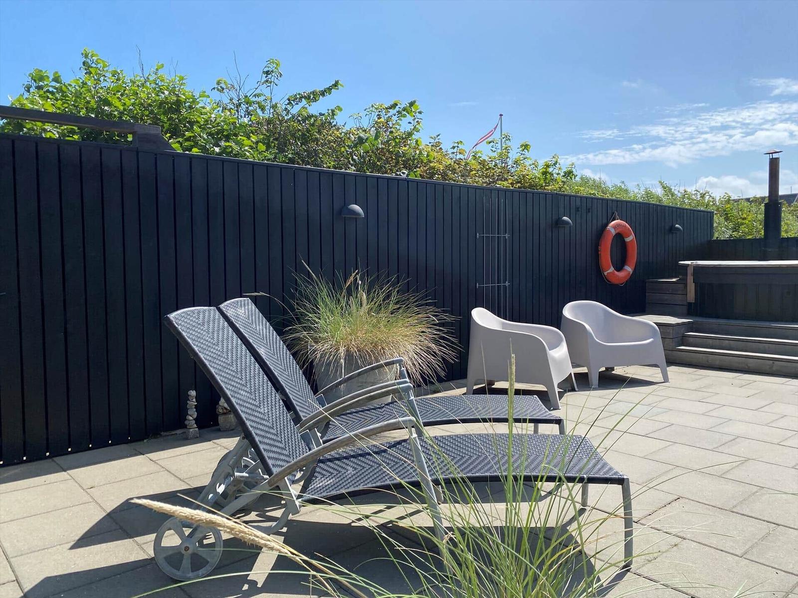 Terrasse mit Liegestühlen, Sitzgelegenheiten und Pflanzen vor dunkler Holzwand.
