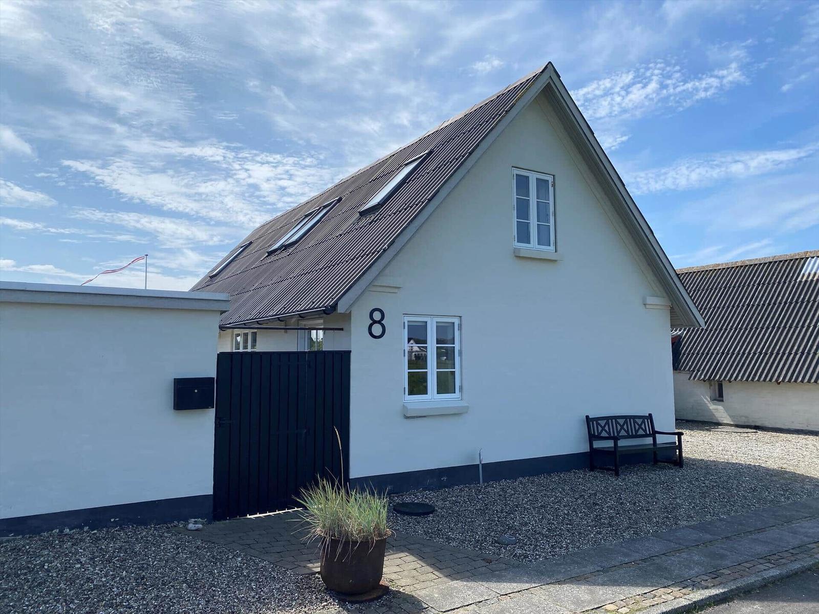 Wohnhaus mit Dachfenstern, schwarzer Tür und Bank auf Kiesfläche.