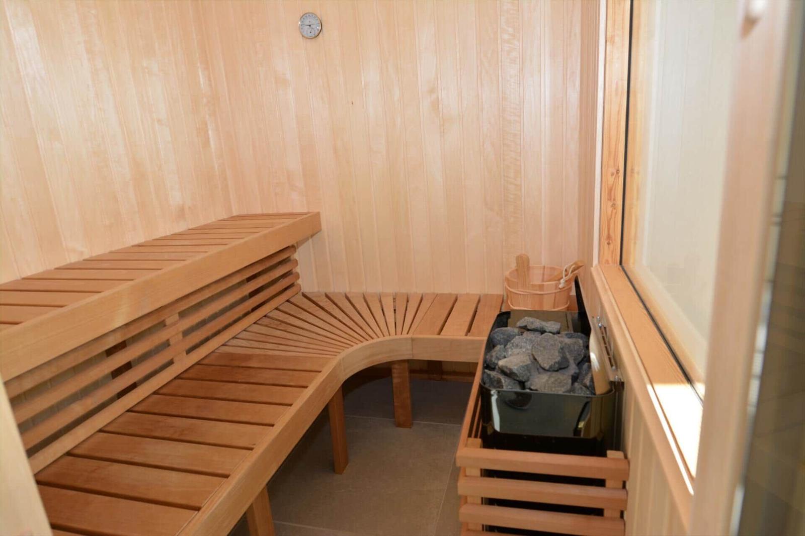 Sauna mit Holzbank, Steinkasten und Uhr an der Wand.