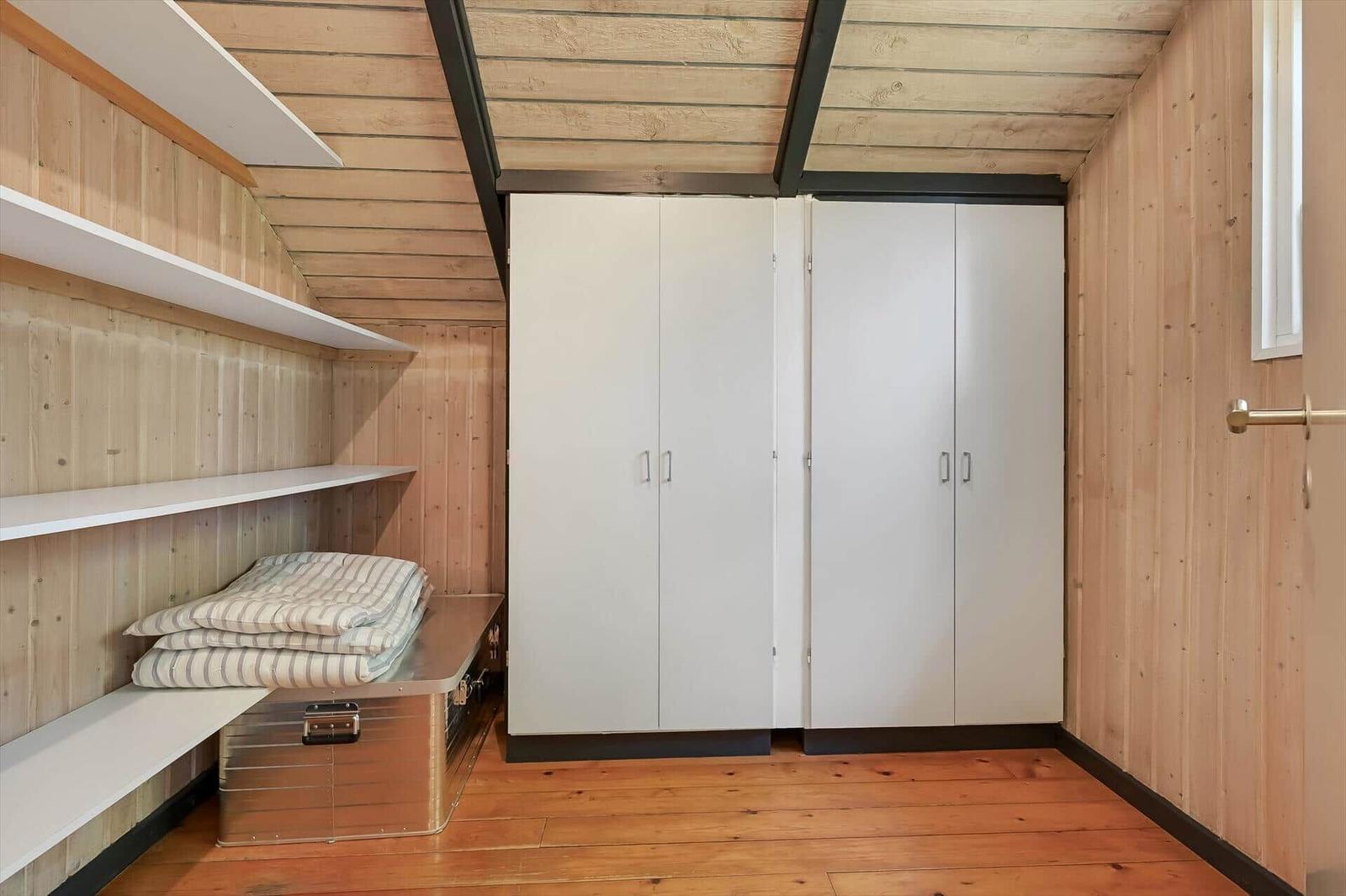 Schlafzimmer mit Holzwand, weißen Schränken und Regalen. Bettbox mit Bettwäsche.