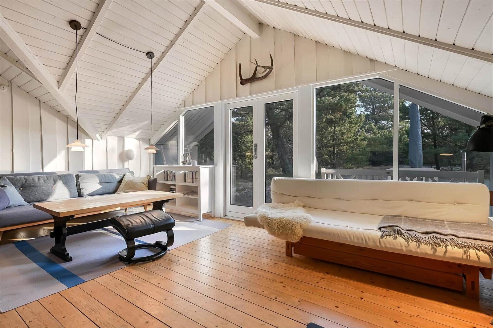 Wohnraum mit Holzboden, Sofa, Couchtisch und großen Fenstern zur Aussicht.