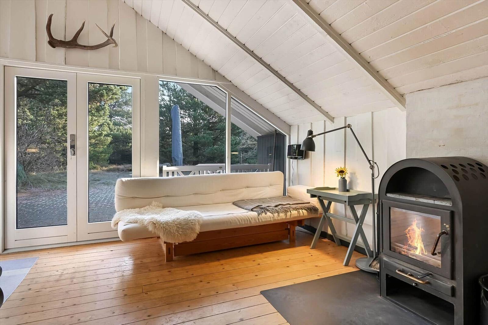 Wohnraum mit Sofa, Kamin und Fenster zur Außenterrasse.