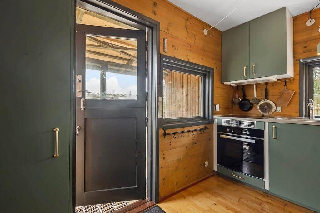 Küche mit grünen Schränken und Holzwand. Tür führt nach draußen.
