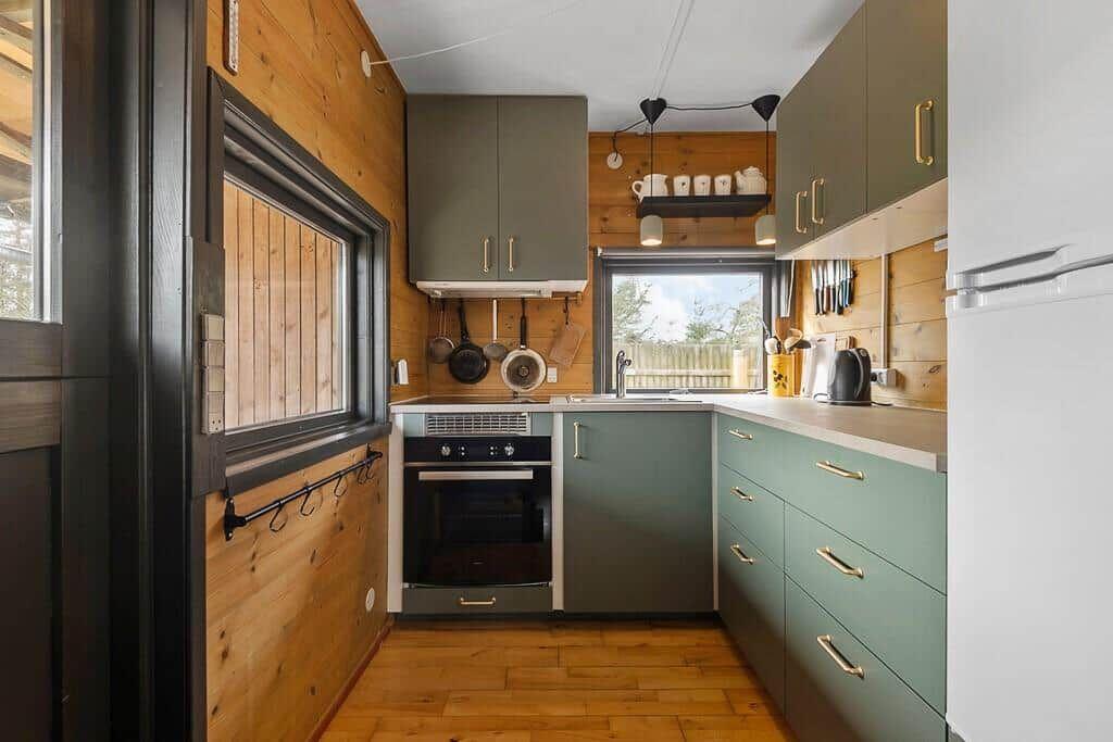 Küche mit Holzwänden, grünen Schränken und Fenster zum Garten.
