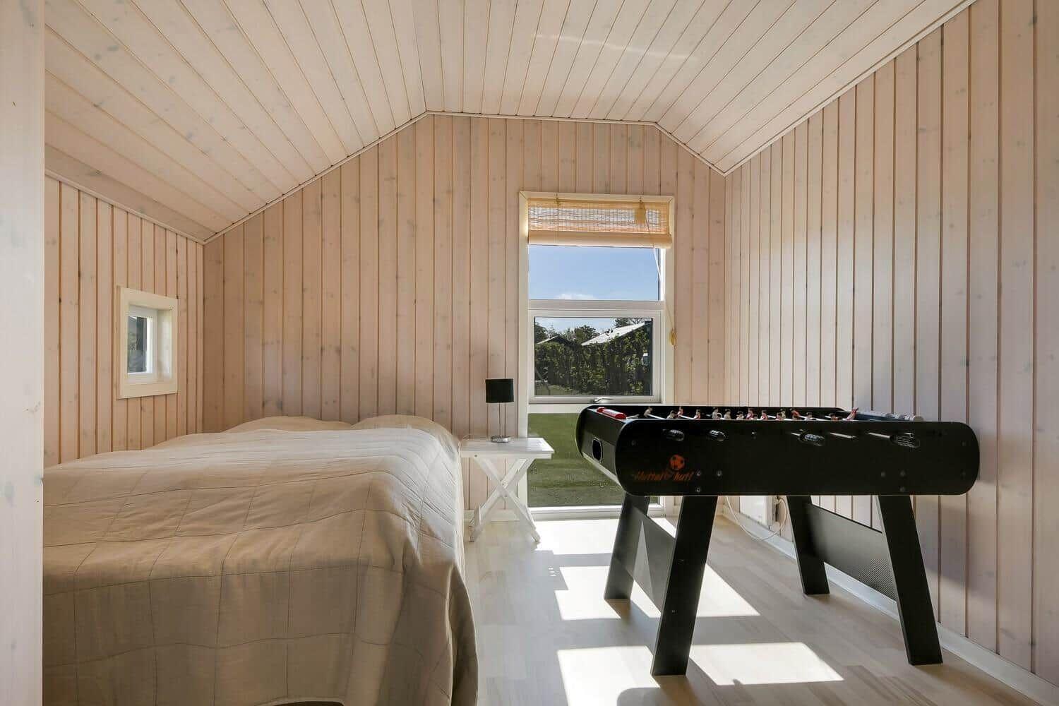 Schlafzimmer mit Bett, Tischfußball und Fenster zum Garten.