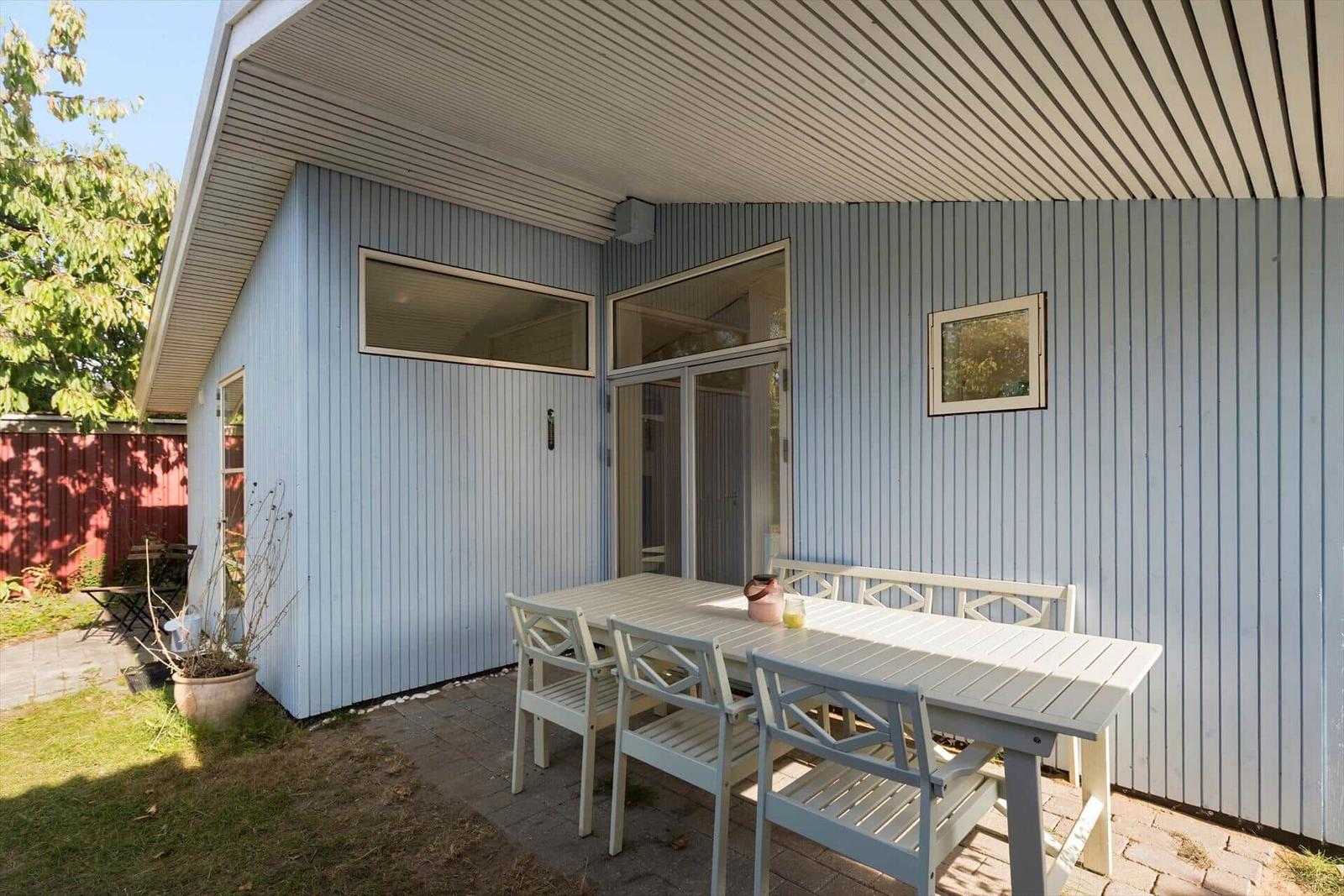 Terrasse mit Tisch und Stühlen vor einem blauen Haus mit Glastüren.