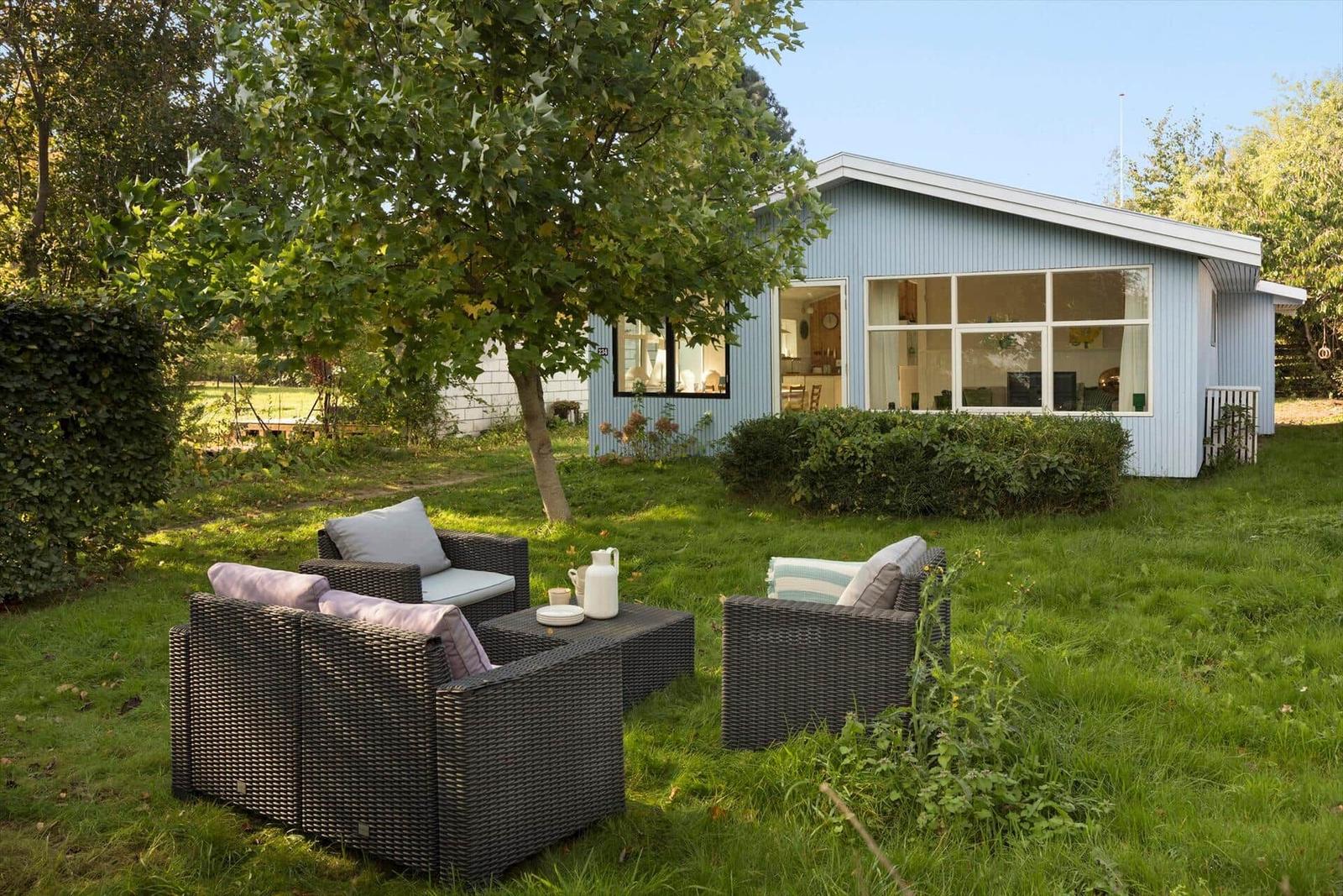 Garten mit Sitzgruppe vor einem blauen Haus mit großen Fenstern.