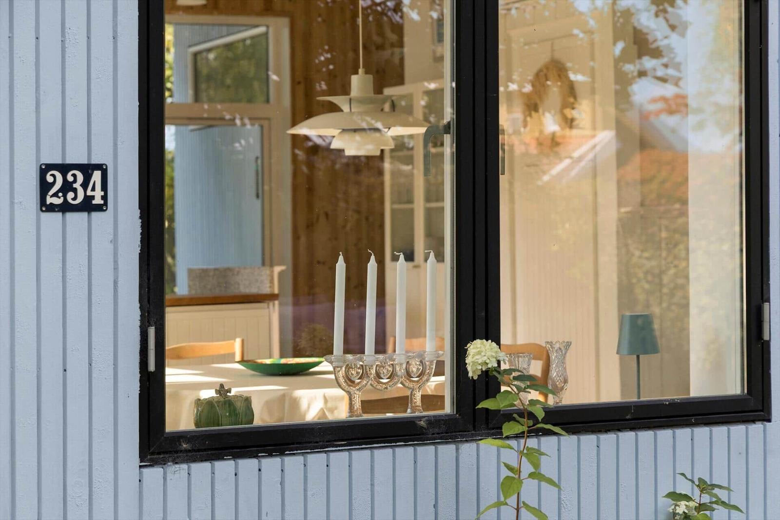 Fensterblick in ein Haus mit Tisch, Kerzen und Blumen. Hausnummer 234 an der Fassade.