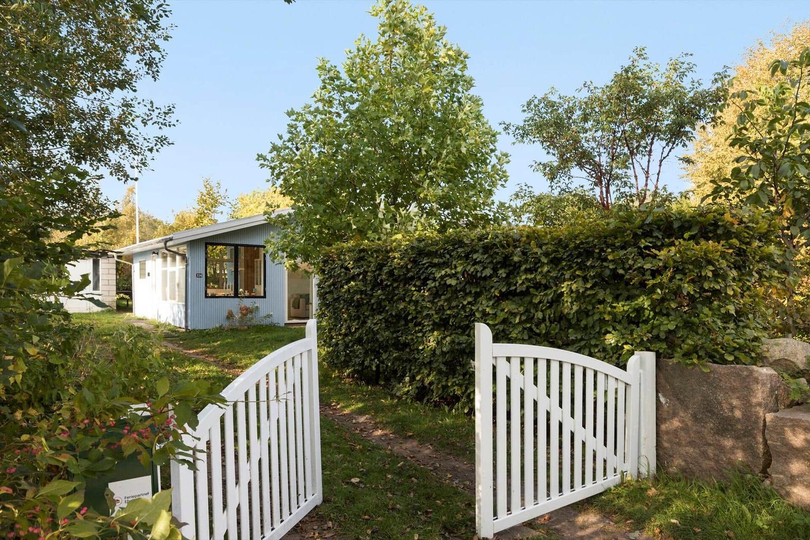Ein blaues Ferienhaus mit weißem Tor und grüner Hecke.