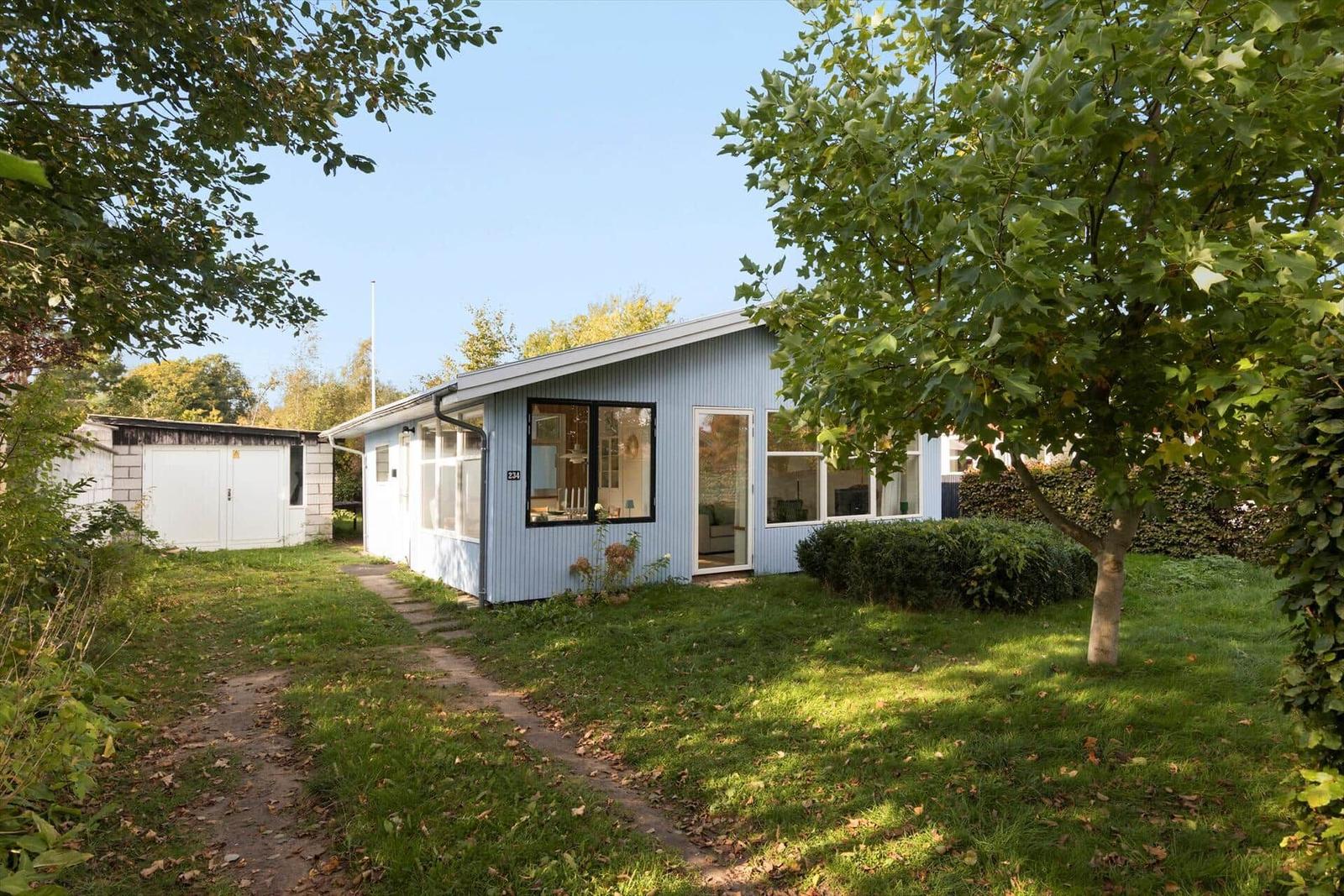 Ein hellblaues Haus mit großen Fenstern und einem Garten. Ein Weg führt zum Eingang.