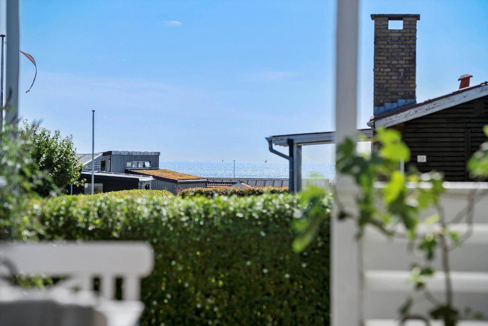 Blick auf das Meer von einem Balkon mit Hecke und Gartenmöbeln.