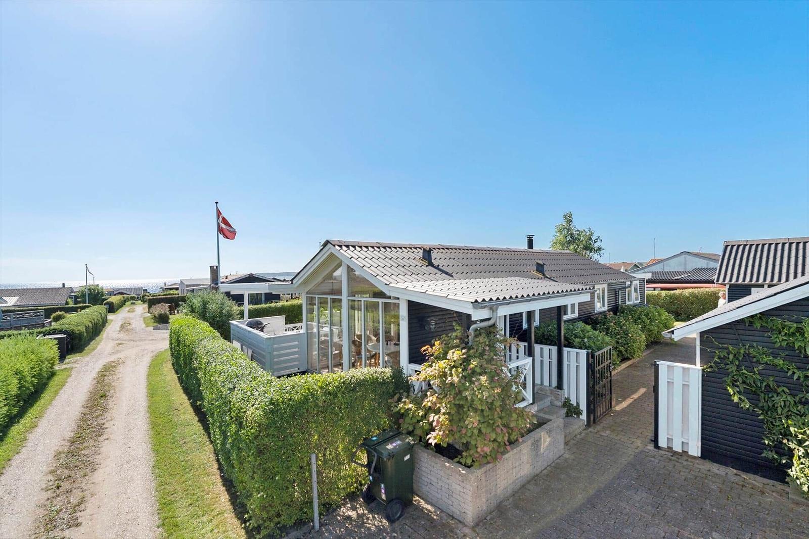 Haus mit Terrasse und Gartenzaun, daneben Flagge und Blick auf Meer