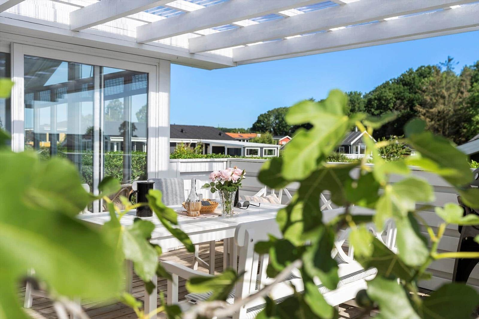 Terrasse mit weißem Tisch und Stühlen unter Pavillon. Blick auf Wohnhäuser und Bäume.