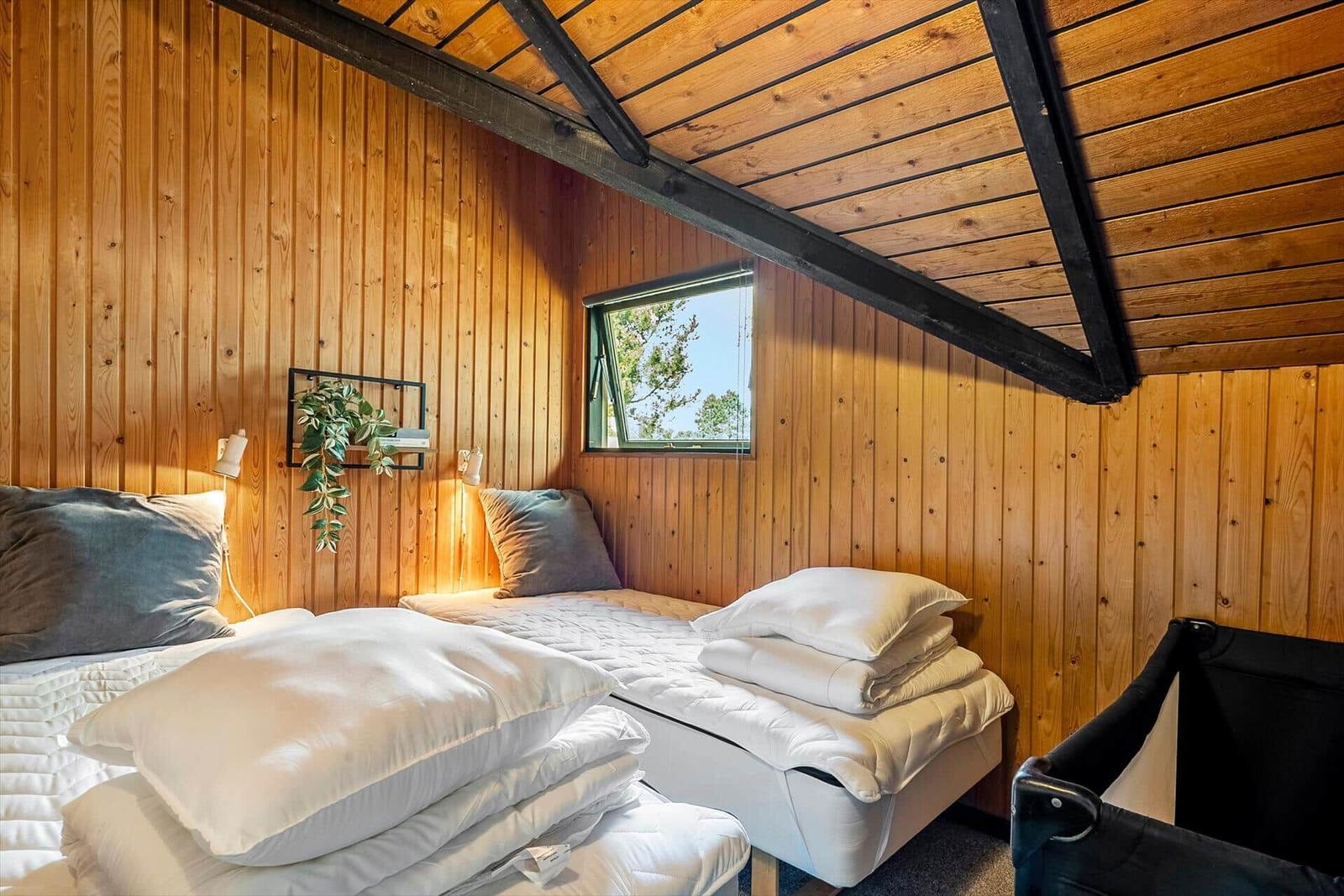 Zwei Betten in einem Holzhaus mit Dachschrägen und kleinem Fenster.