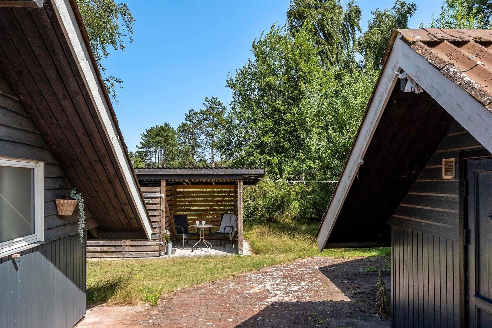 Zwei Holzhäuser mit Terrasse und Gartenbereich. Holzterrasse mit Tisch und Stühlen.