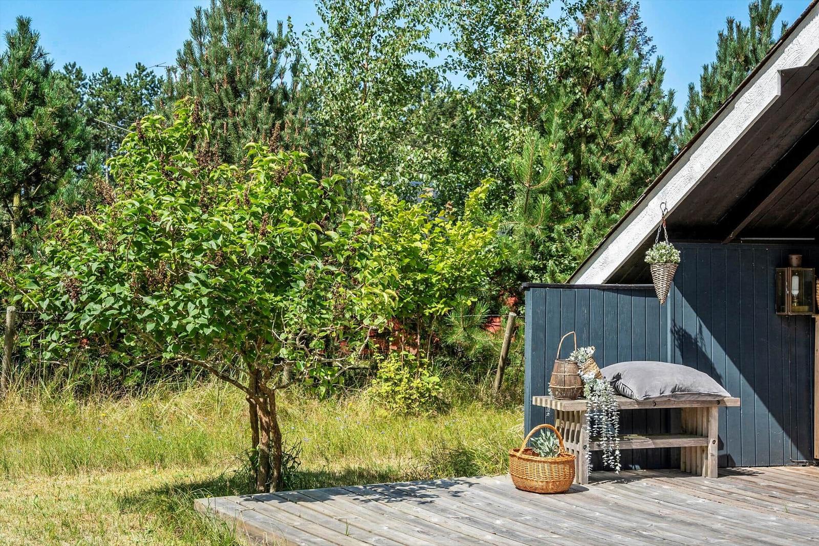 Holzterrasse mit Bank, Körben und Pflanzen vor einem Haus mit dunklem Holzverkleidung.