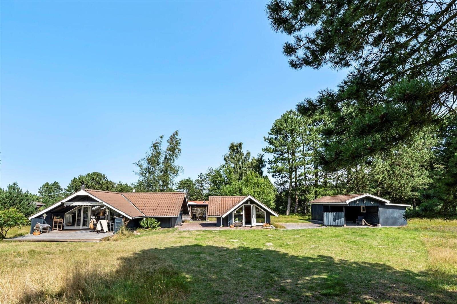 Haus mit Terrasse, Garten und Bäumen unter blauem Himmel.