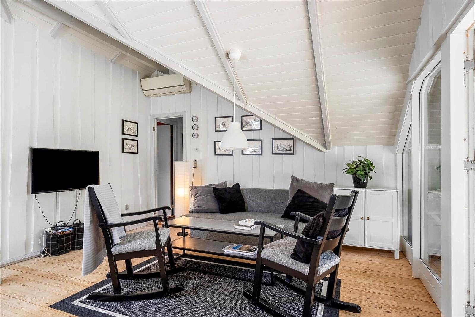 Wohnzimmer mit Sofa, zwei Sessel, Fernseher und Holzboden.