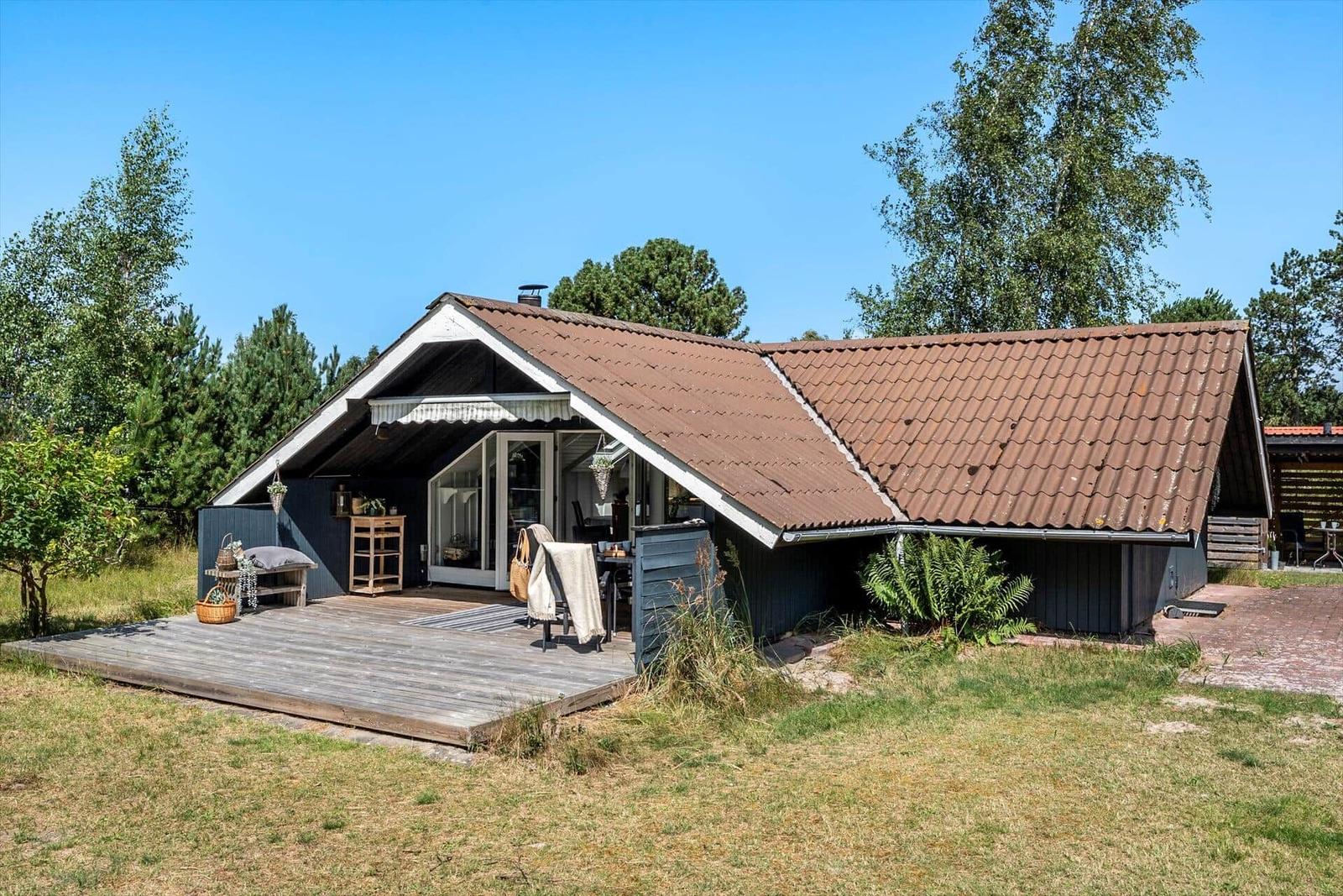Ein Ferienhaus mit Holzterrasse und braunem Dach unter blauem Himmel.