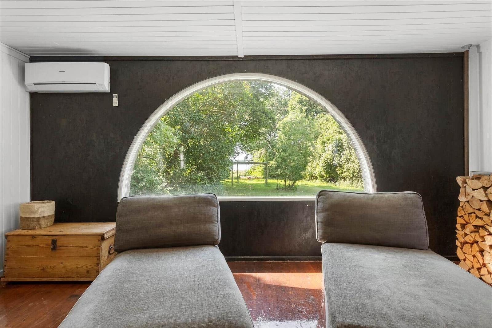 Zwei Liegen vor großem Bogenfenster mit Blick auf grüne Landschaft.