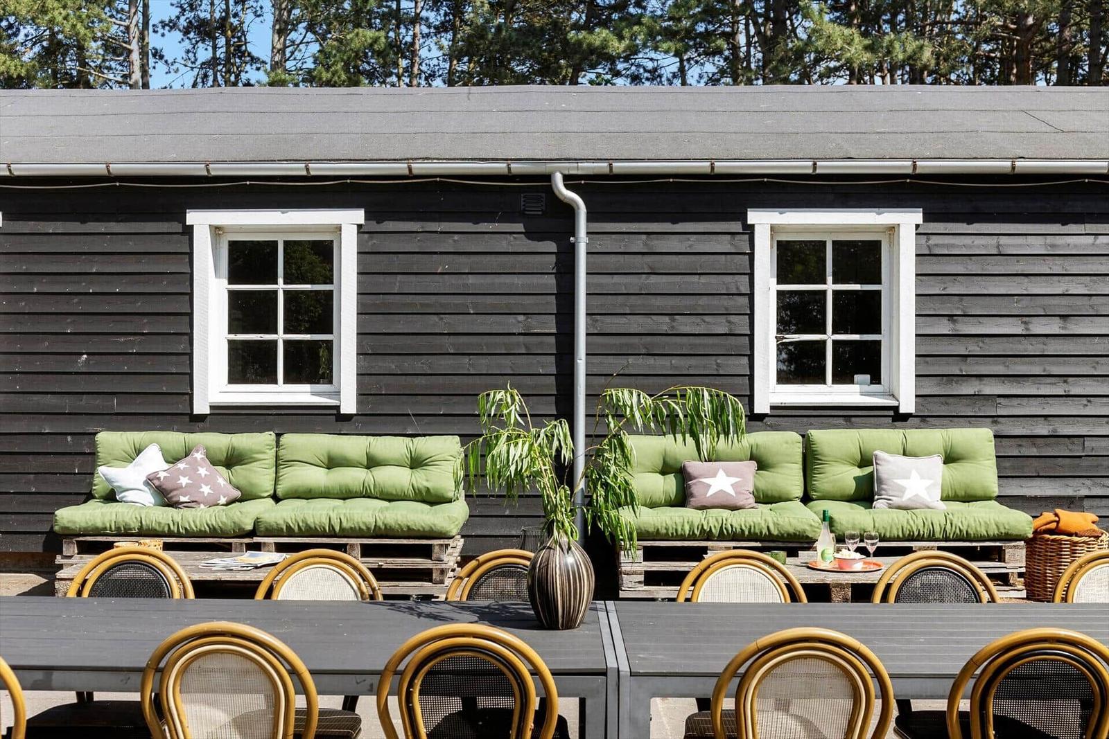 Außenbereich mit grünen Sofas, Tisch und Stühlen vor einem dunklen Holzhaus.