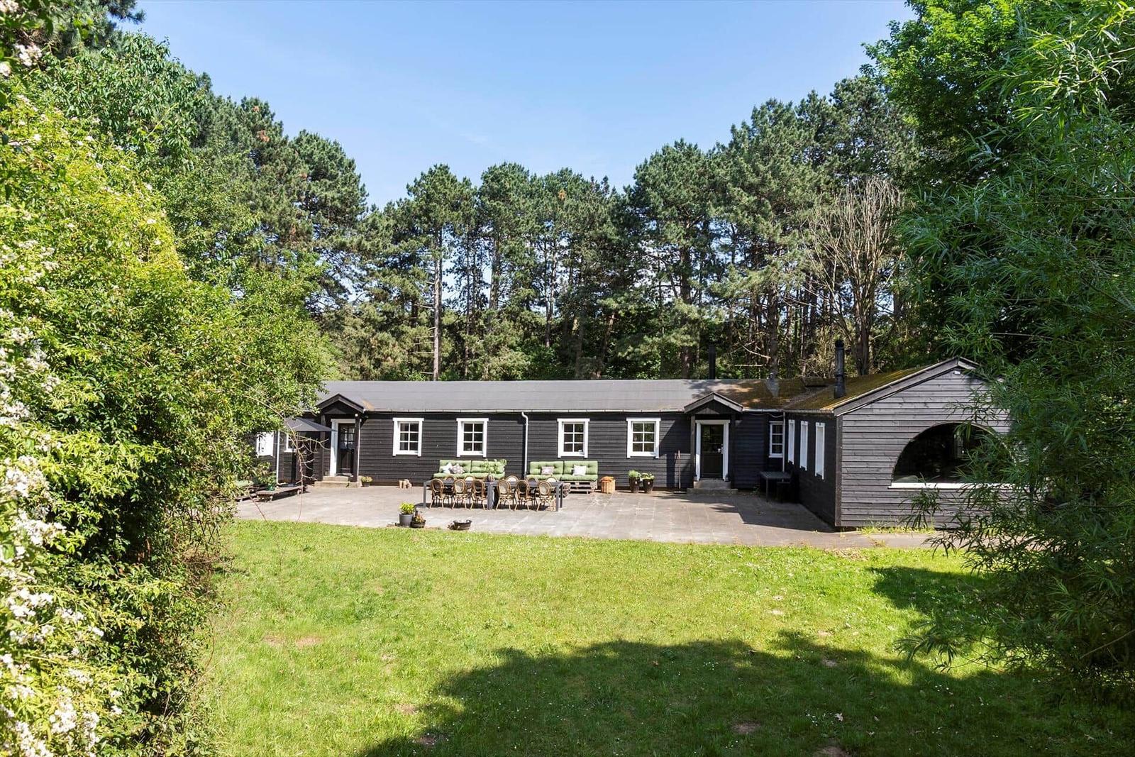 Schwarzes Holzhaus mit Terrasse, Garten und Wald im Hintergrund.