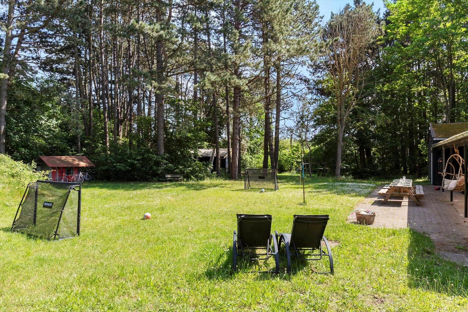 Grüner Garten mit Liegestühlen, Tisch und Grillplatz neben Wald.