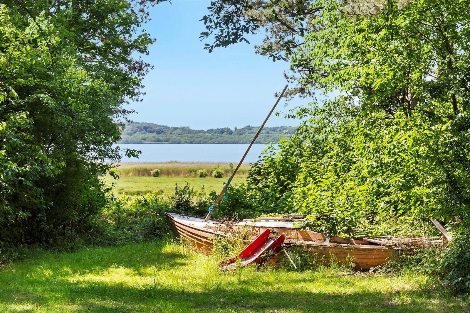 Ein rotes Ruderboot liegt im Gras neben einem See, umgeben von Bäumen.