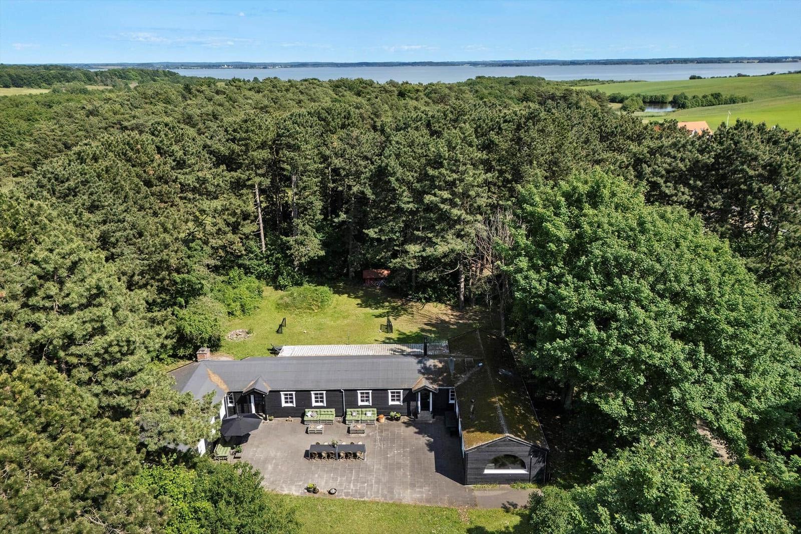 Schwarze Hütte mit Terrasse im Wald, Blick auf Wasser.