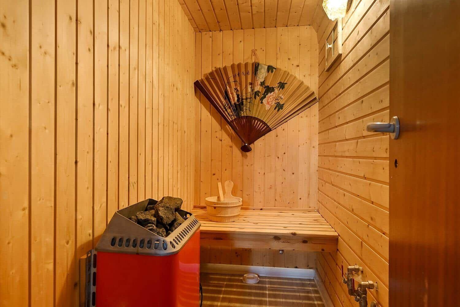 Sauna mit Holzwand, Sitzbank, Badeeimer und dekorativem Fächer.